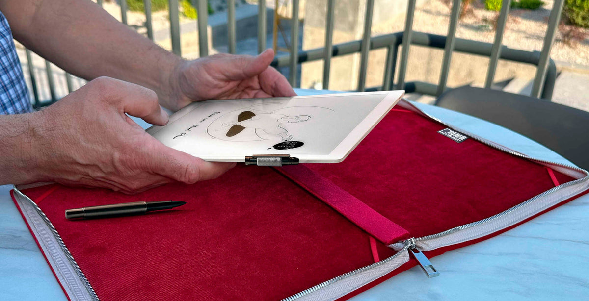 Hands placing a Supernote A5 X2 Manta e-ink into a red velvet-lined zippered folio case on a round outdoor table, with a pen resting inside the case for writing use.
